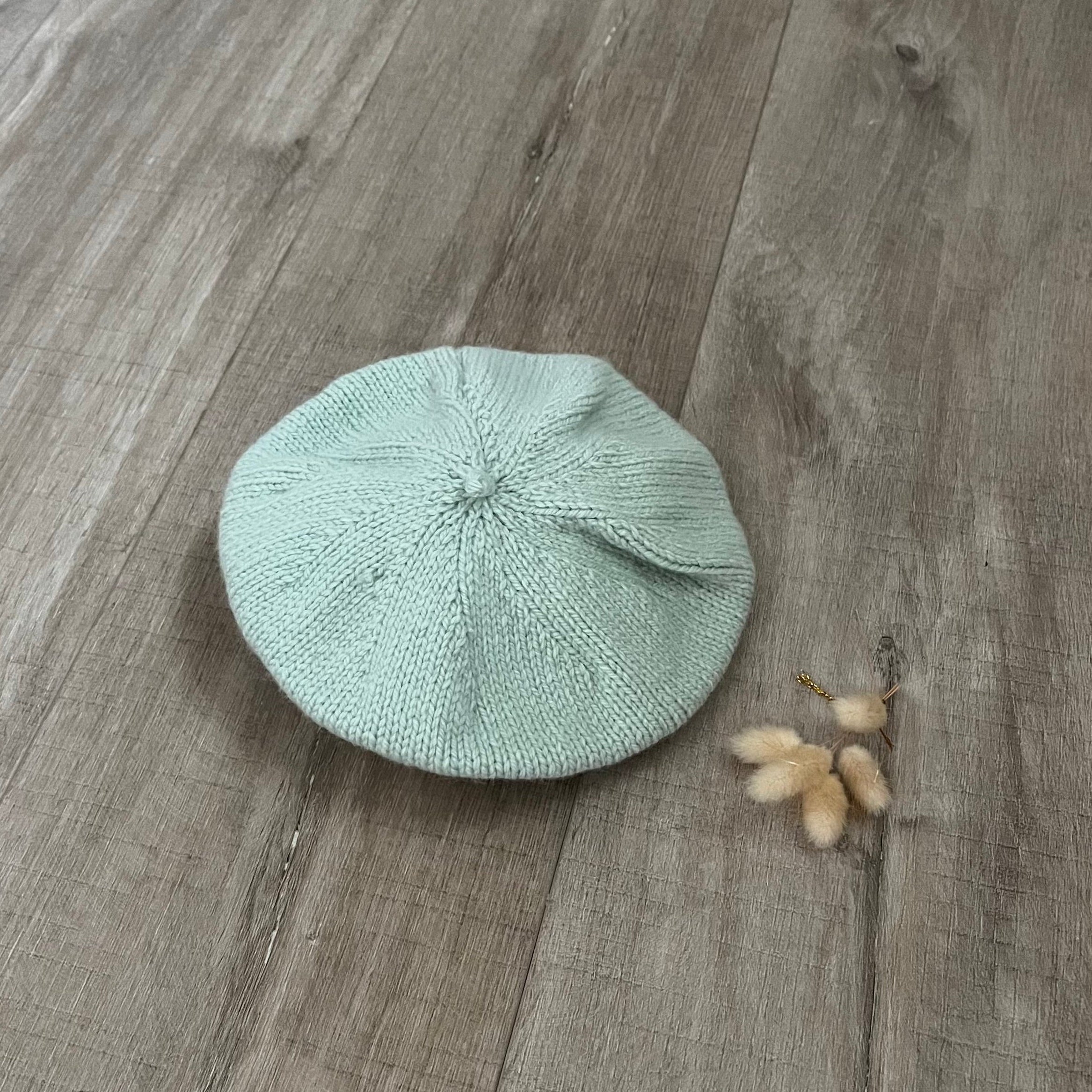 mint green beret on a wooden surface with dried flowers