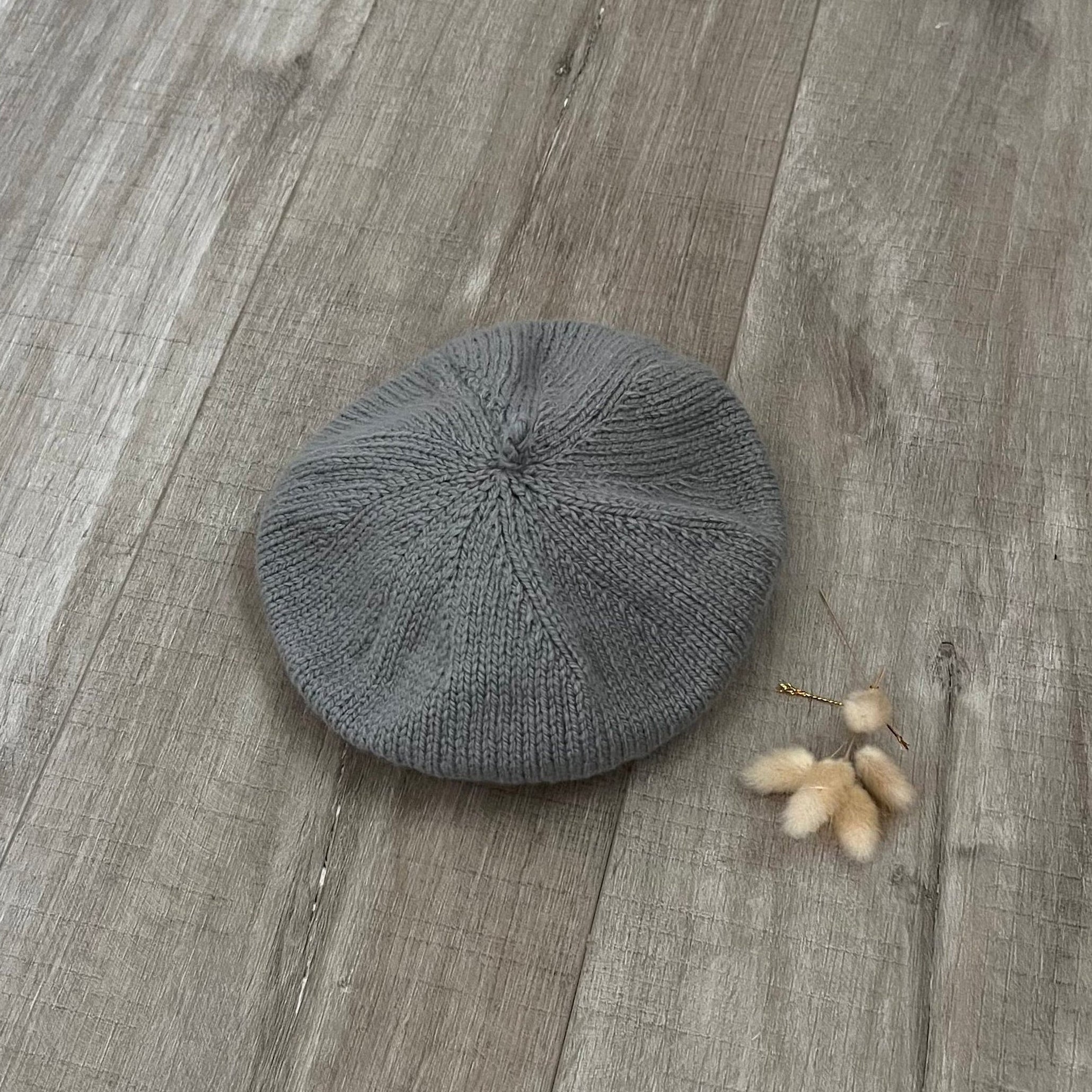 mushroom knit beret on a wooden surface with a small branch of cotton.