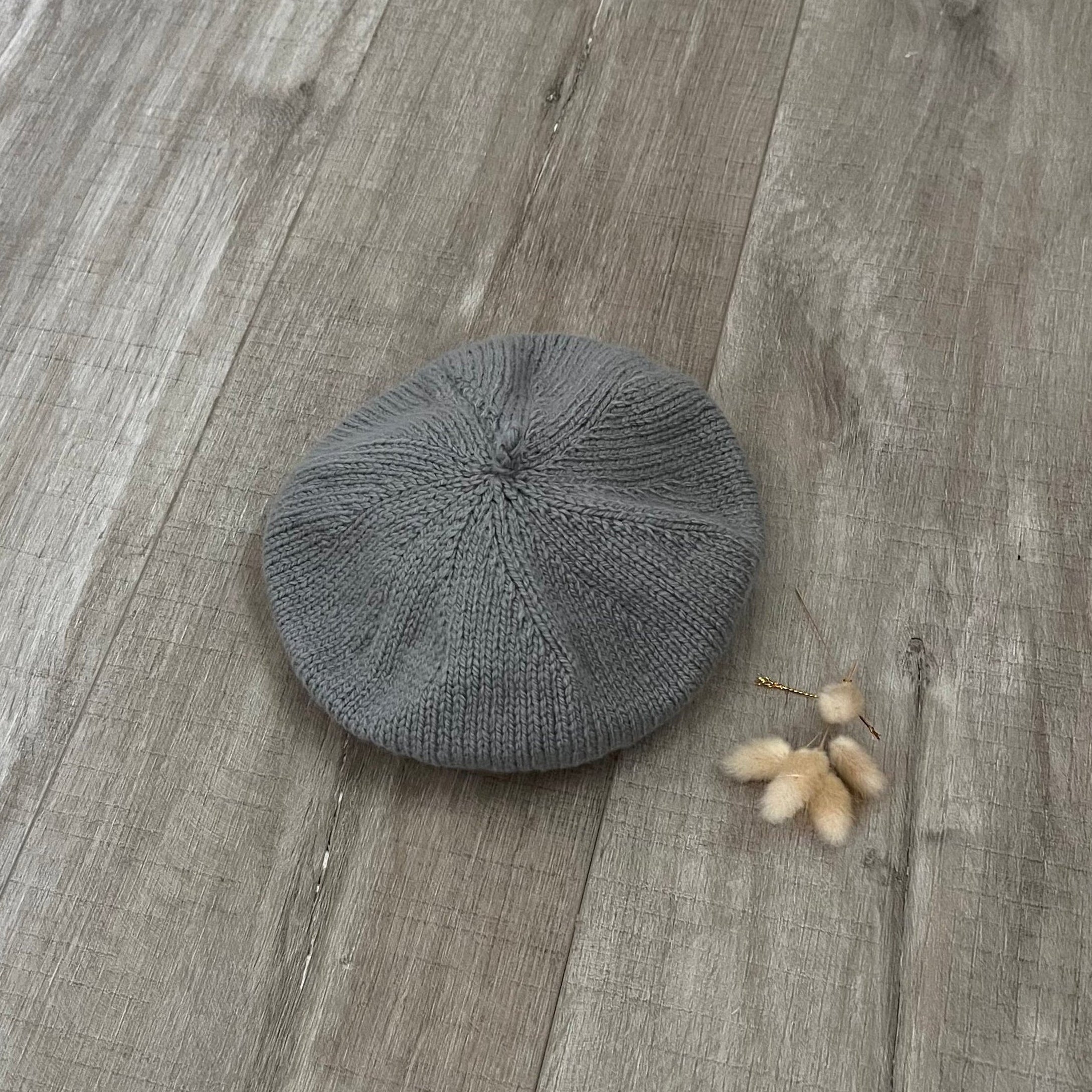 mushroom knit beret on a wooden surface with a small branch of cotton.
