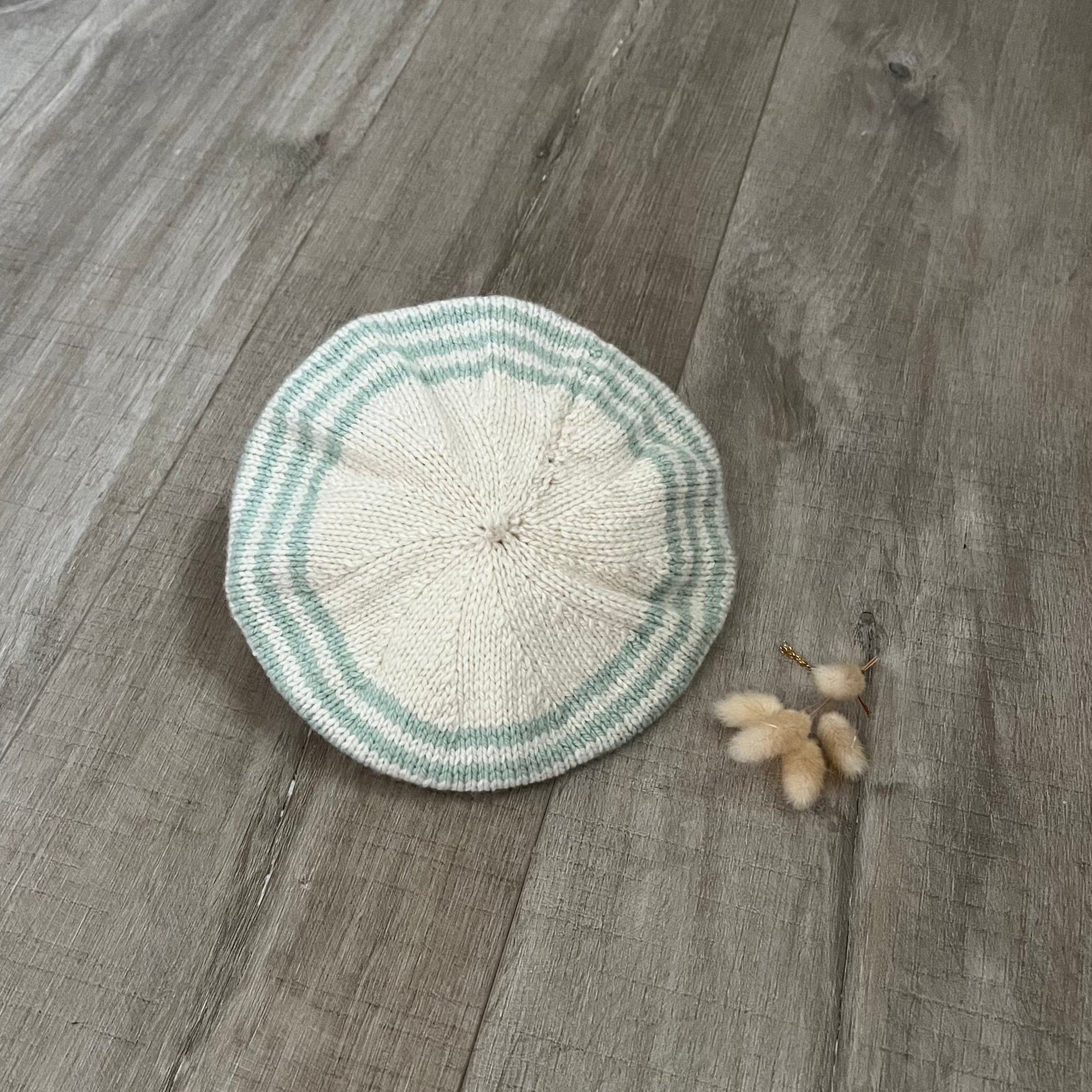 Knitted beret with green and white stripes on a wooden surface