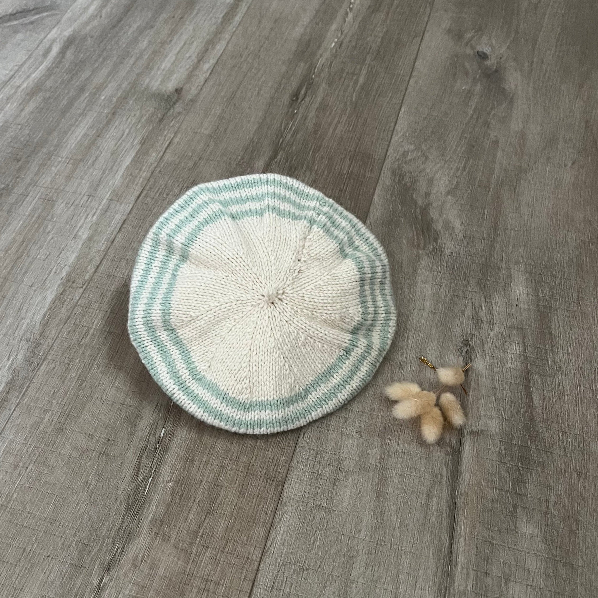 Knitted beret with green and white stripes on a wooden surface