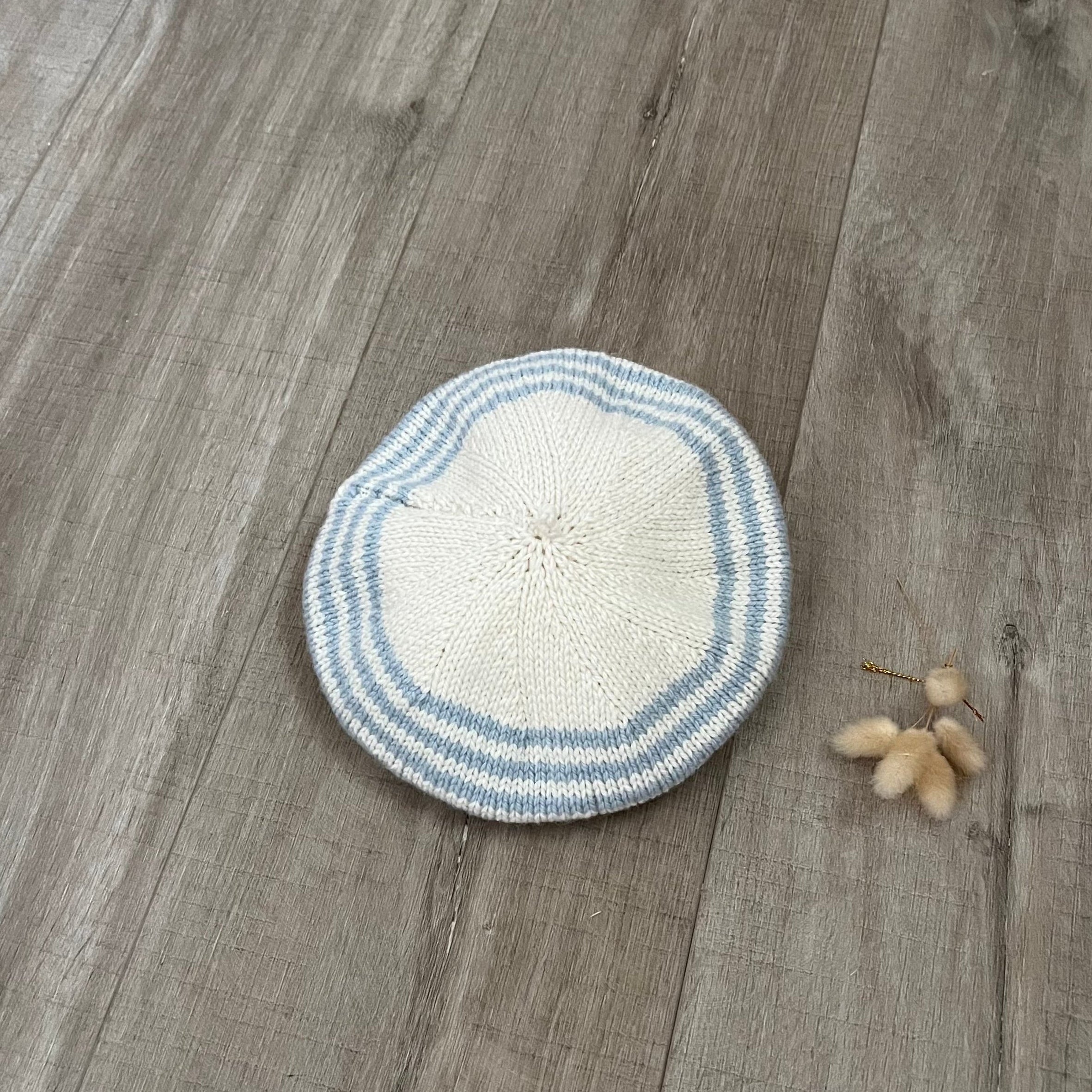 Knitted beret with blue and white stripes on a wooden surface