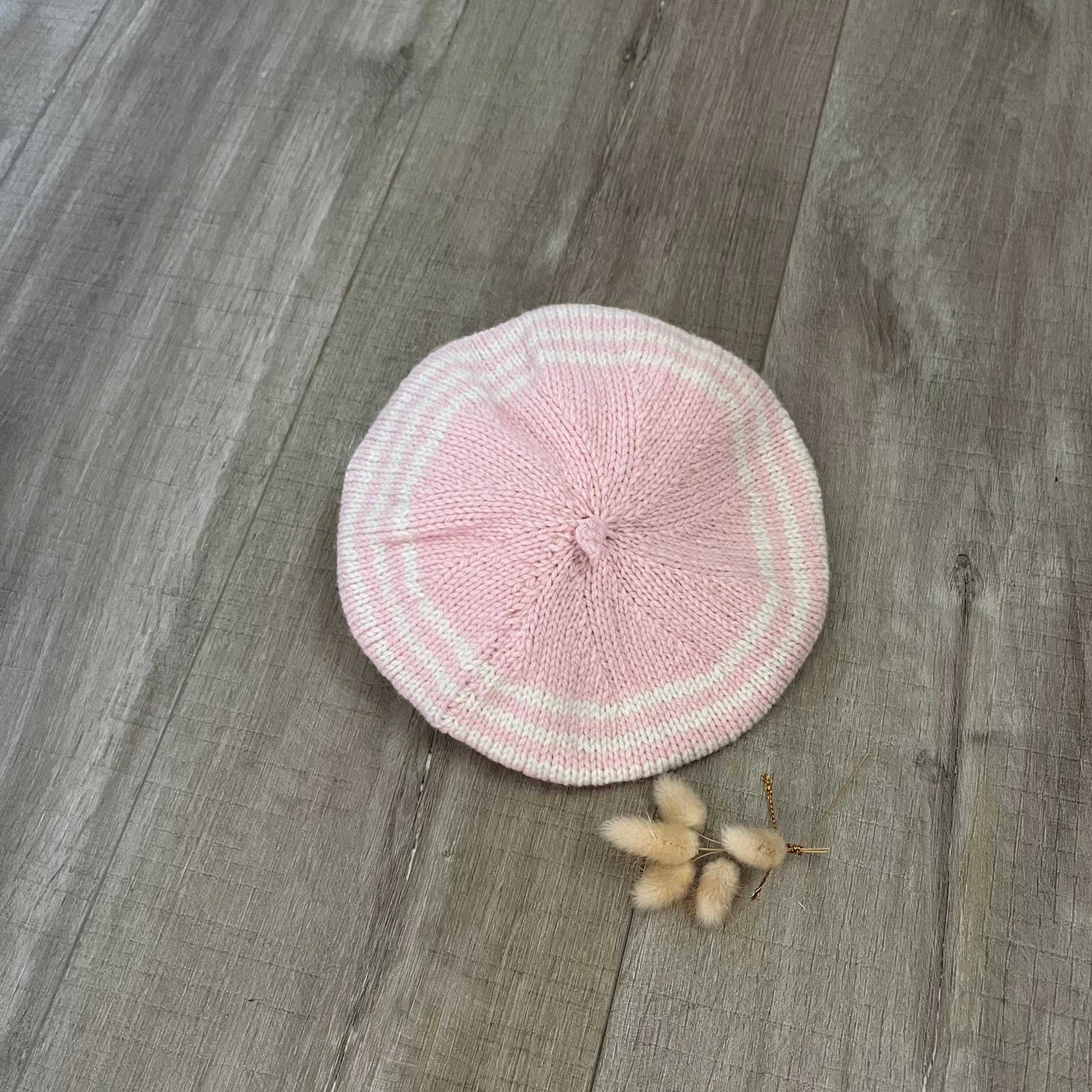 Pink stripe knitted beret on a wooden surface with dried flowers.