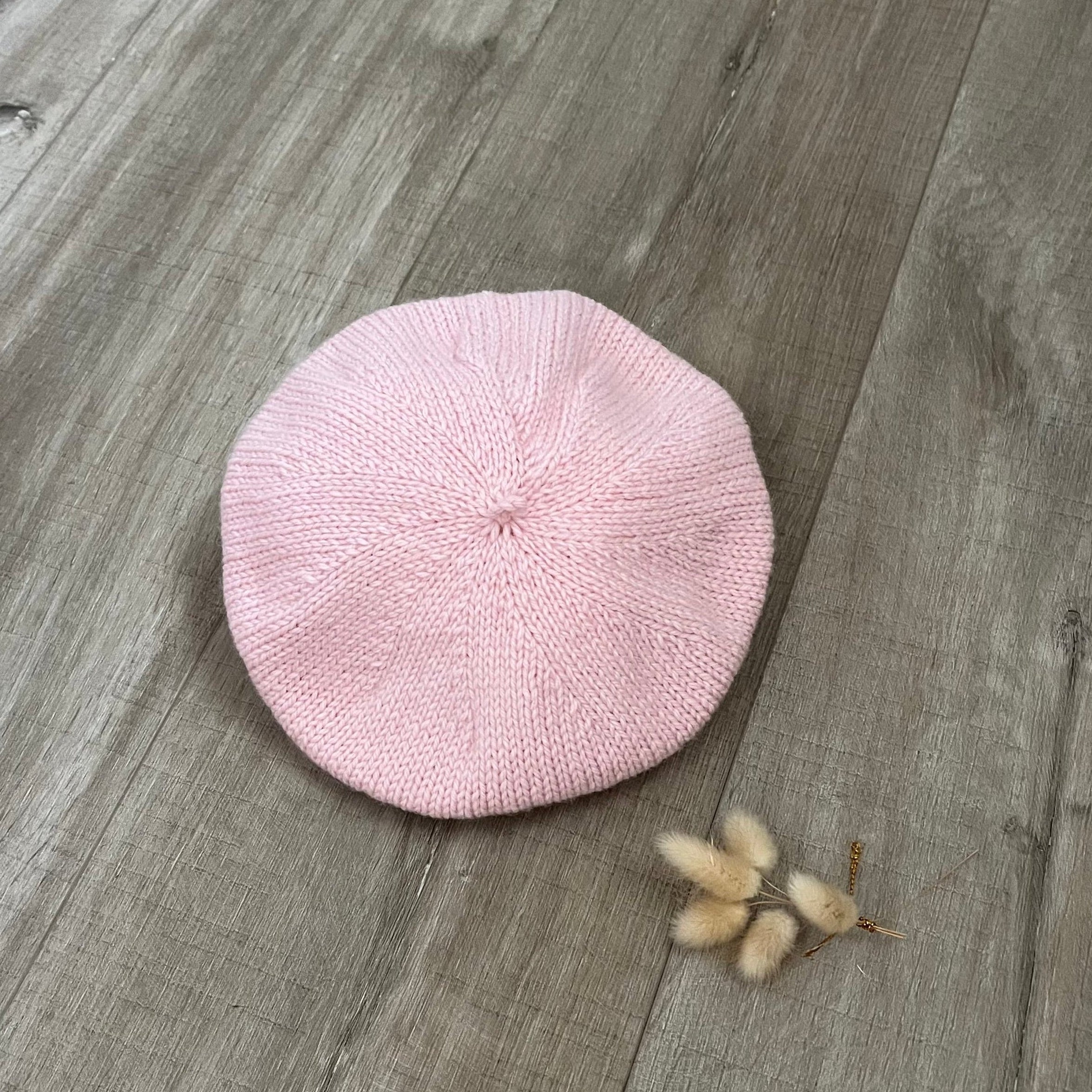 Pink knitted beret on a wooden surface with dried flower