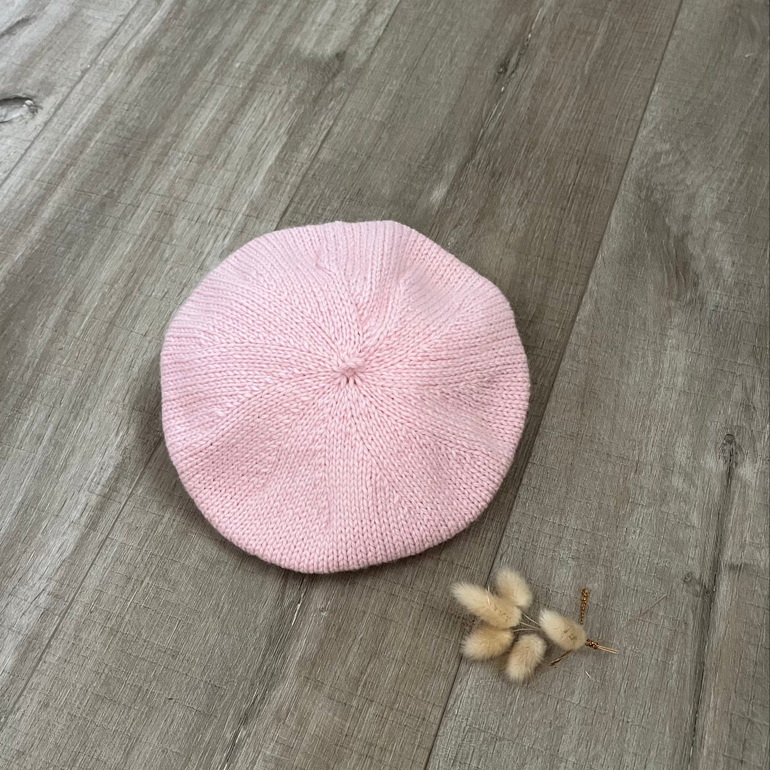 Pink knitted beret on a wooden surface with dried flower