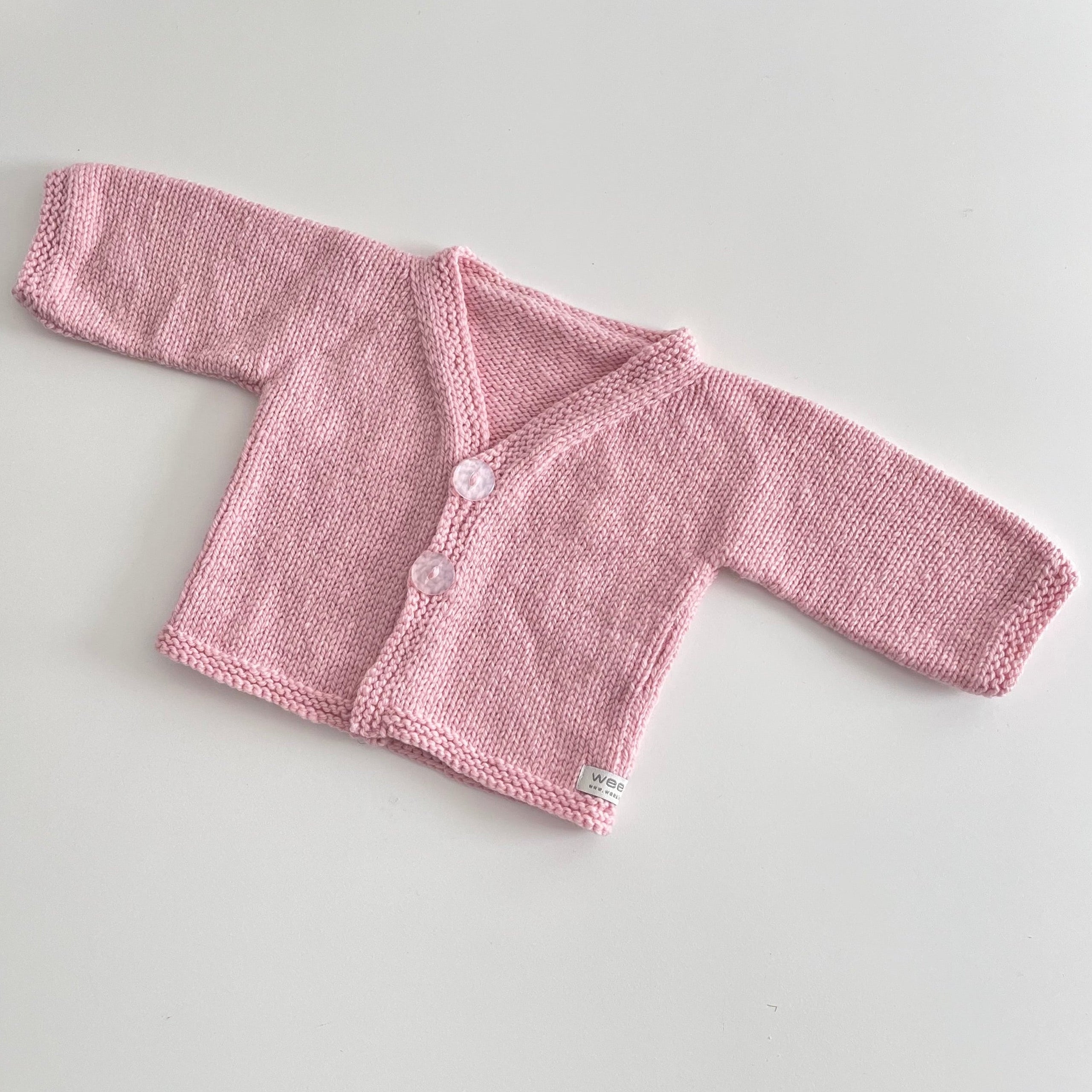 A pink hand-knit baby cardigan  with long sleeves, a V-neck, and two light  buttons, laid flat on a light gray background.