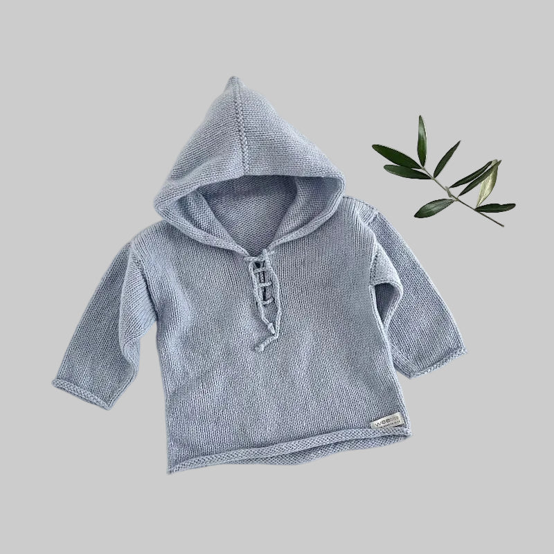 Blue knitted baby hoodie on a light background with a branch of leaves.