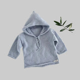Blue knitted baby hoodie on a light background with a branch of leaves.