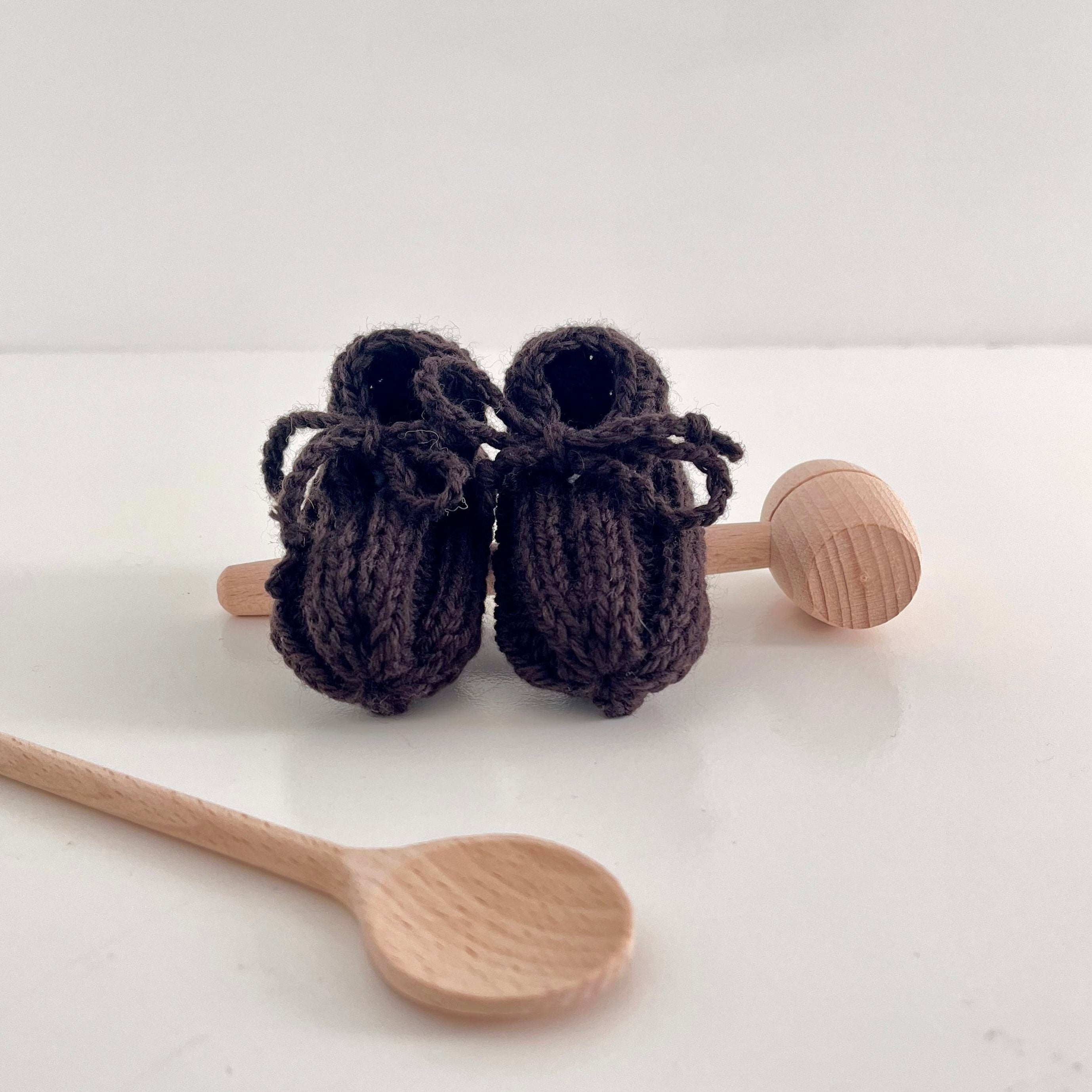 Knitted brown baby booties with wooden spoons on a white background