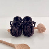 Knitted brown baby booties with wooden spoons on a white background
