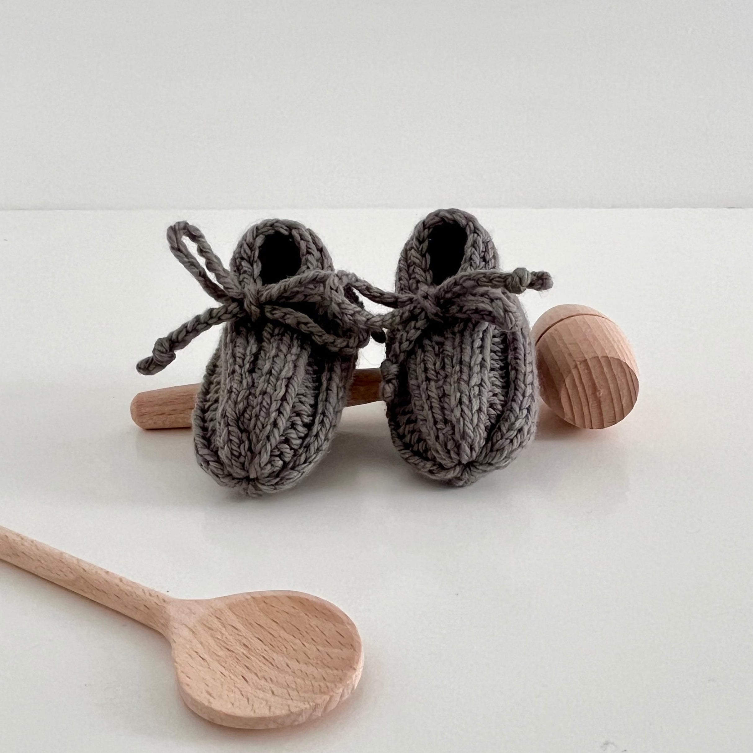 Knitted baby booties with wooden spoons on a white background