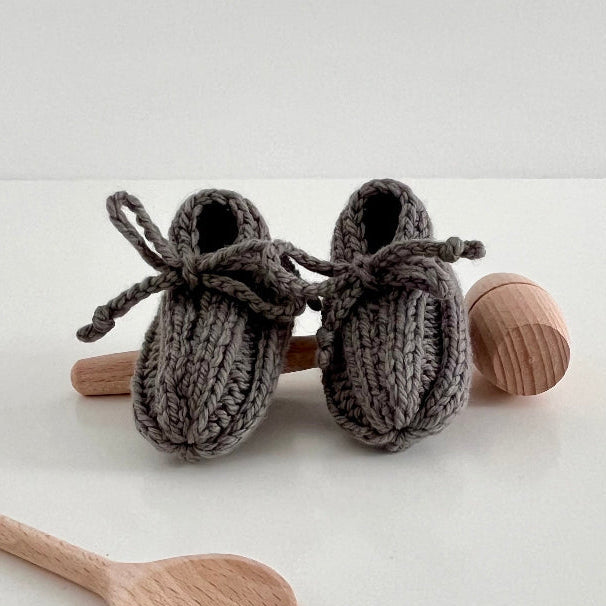 Knitted baby booties with wooden spoons on a white background
