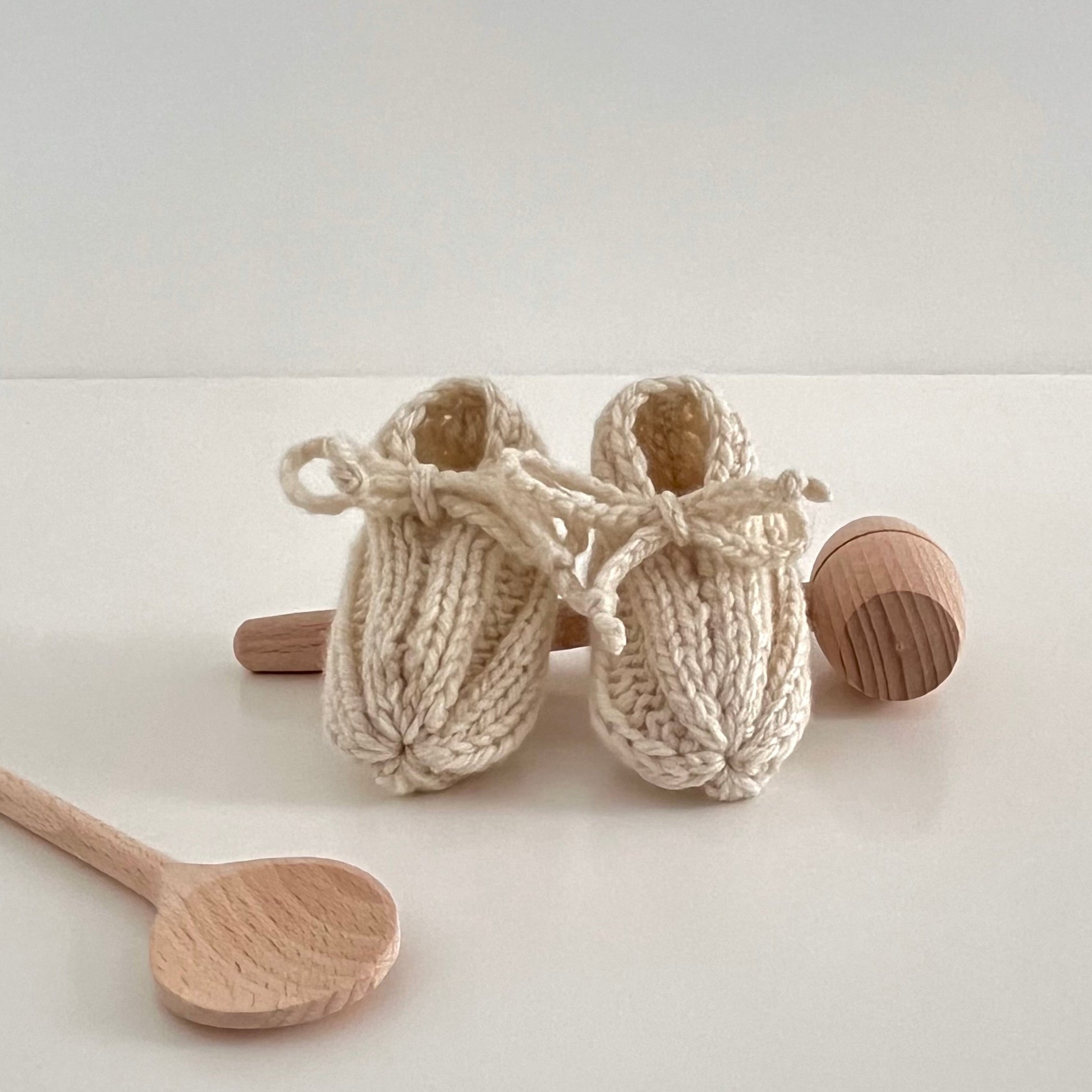 Knitted baby booties with wooden spoons on a light background