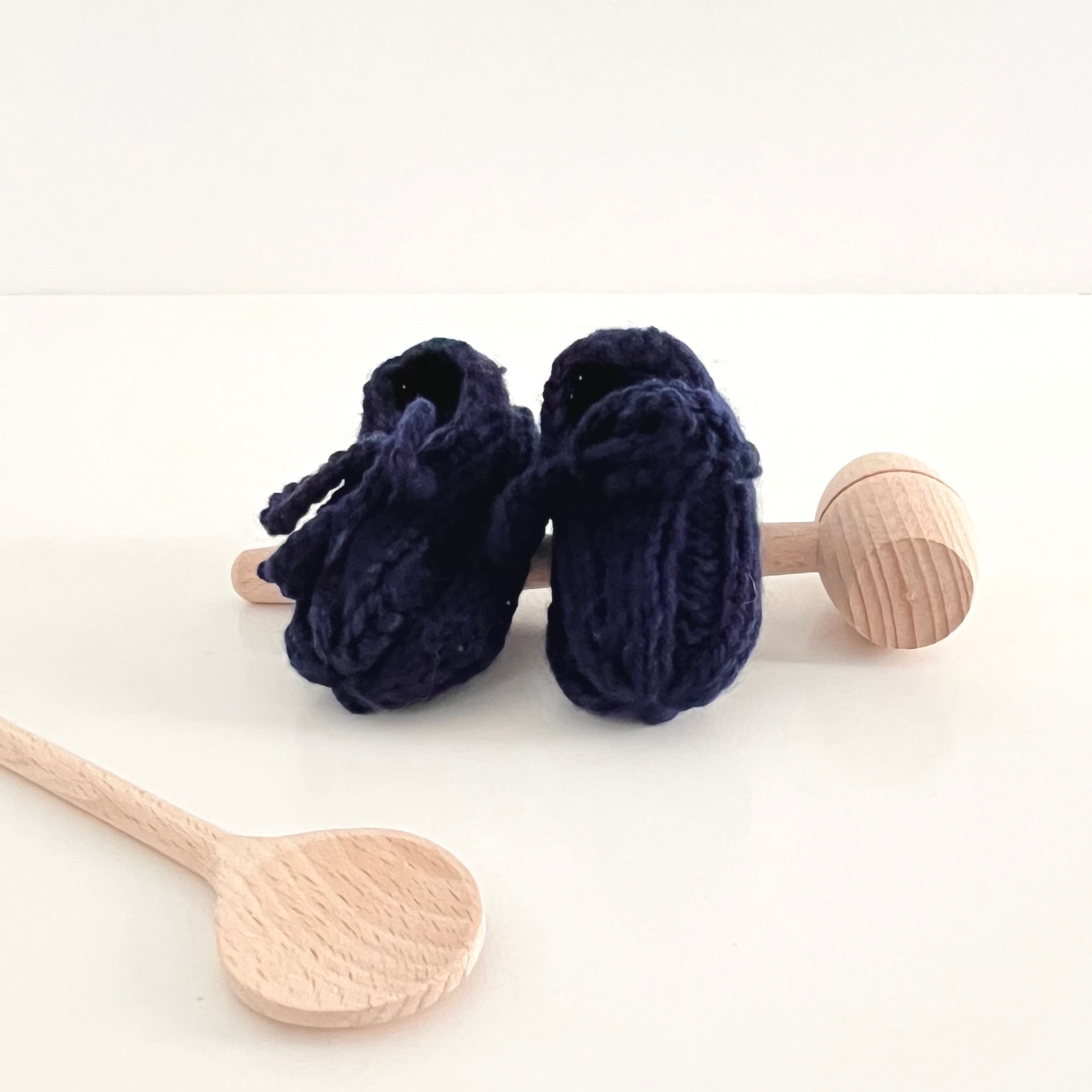Navy blue baby booties with wooden rattle on a white background
