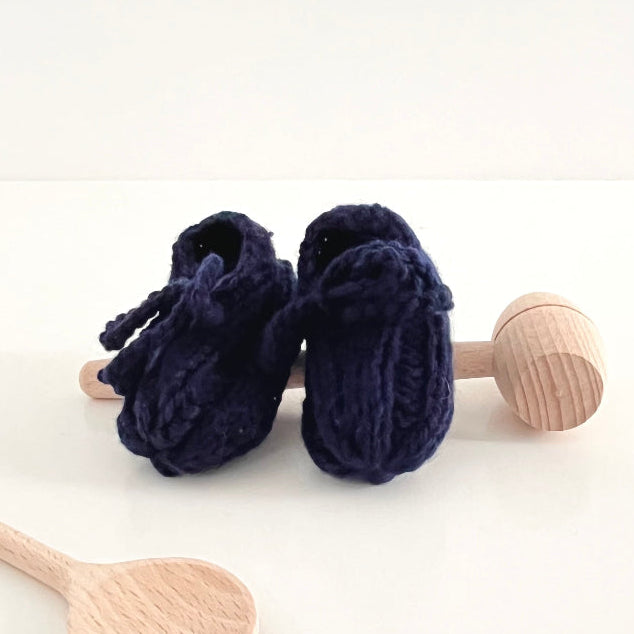 Navy blue baby booties with wooden rattle on a white background