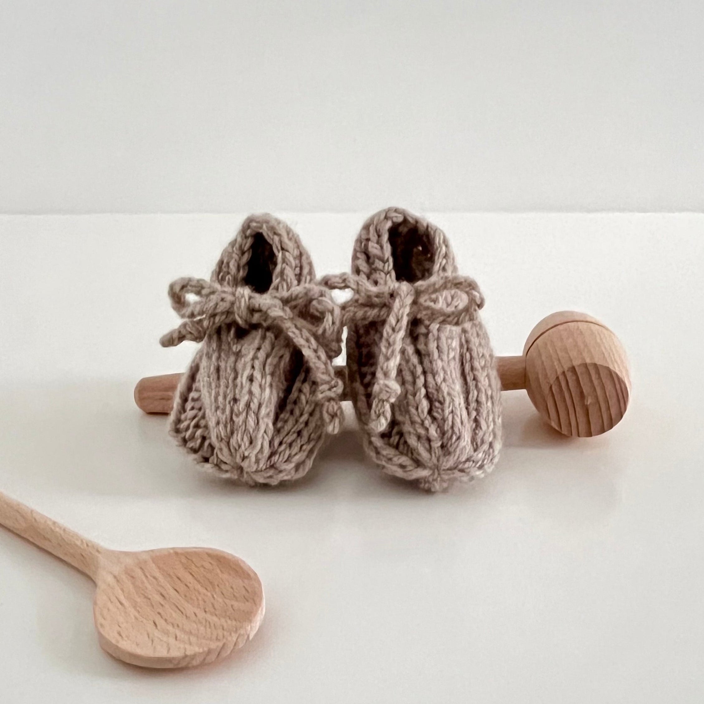 Knitted baby booties with wooden rattle and spoon on a white background