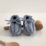 Pair of blue knitted baby booties with wooden spoons on a white background