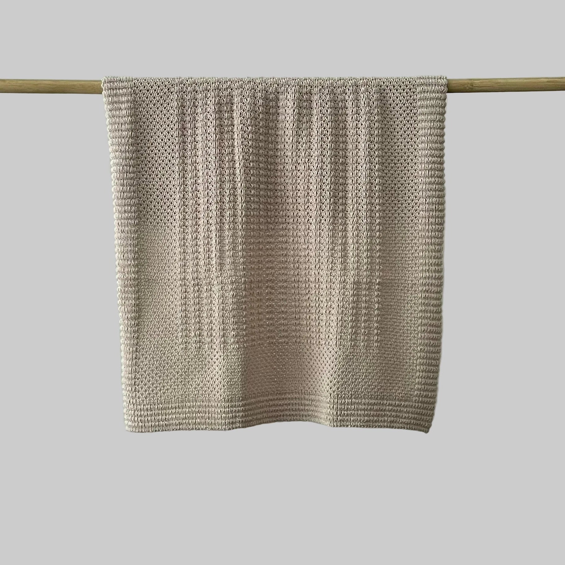 Textured sandstone bassinet blanket hanging on a wooden rod against a grey background
