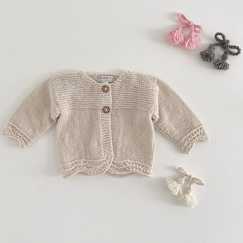 Natural coloured knitted baby cardigan on a light grey background