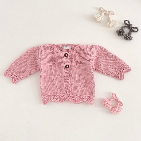 Pink coloured knitted baby cardigan on a light grey background