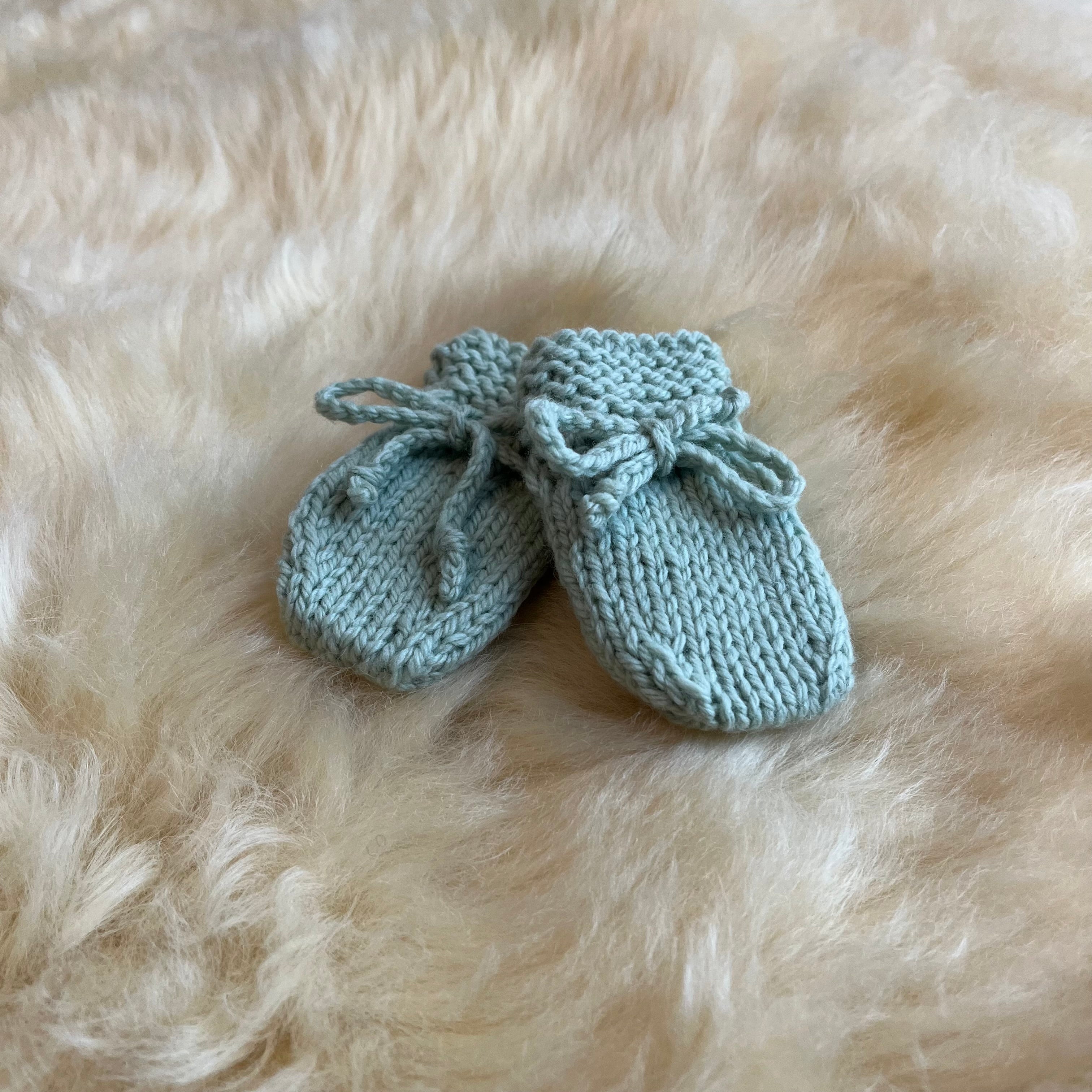 Pair of mint knitted baby mittens on a fluffy sheepskin rug