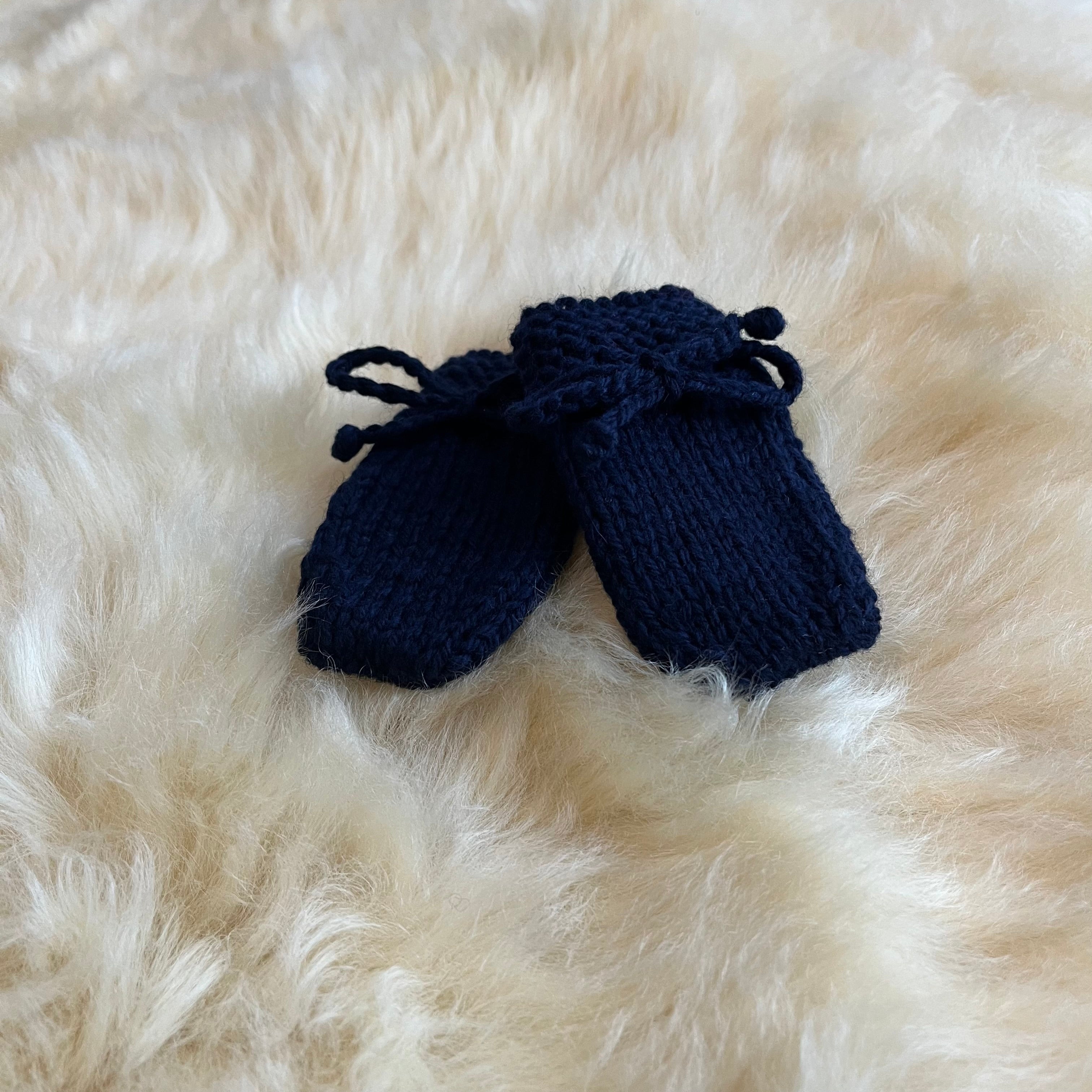 Pair of navy knitted baby mittens on a fluffy sheepskin rug