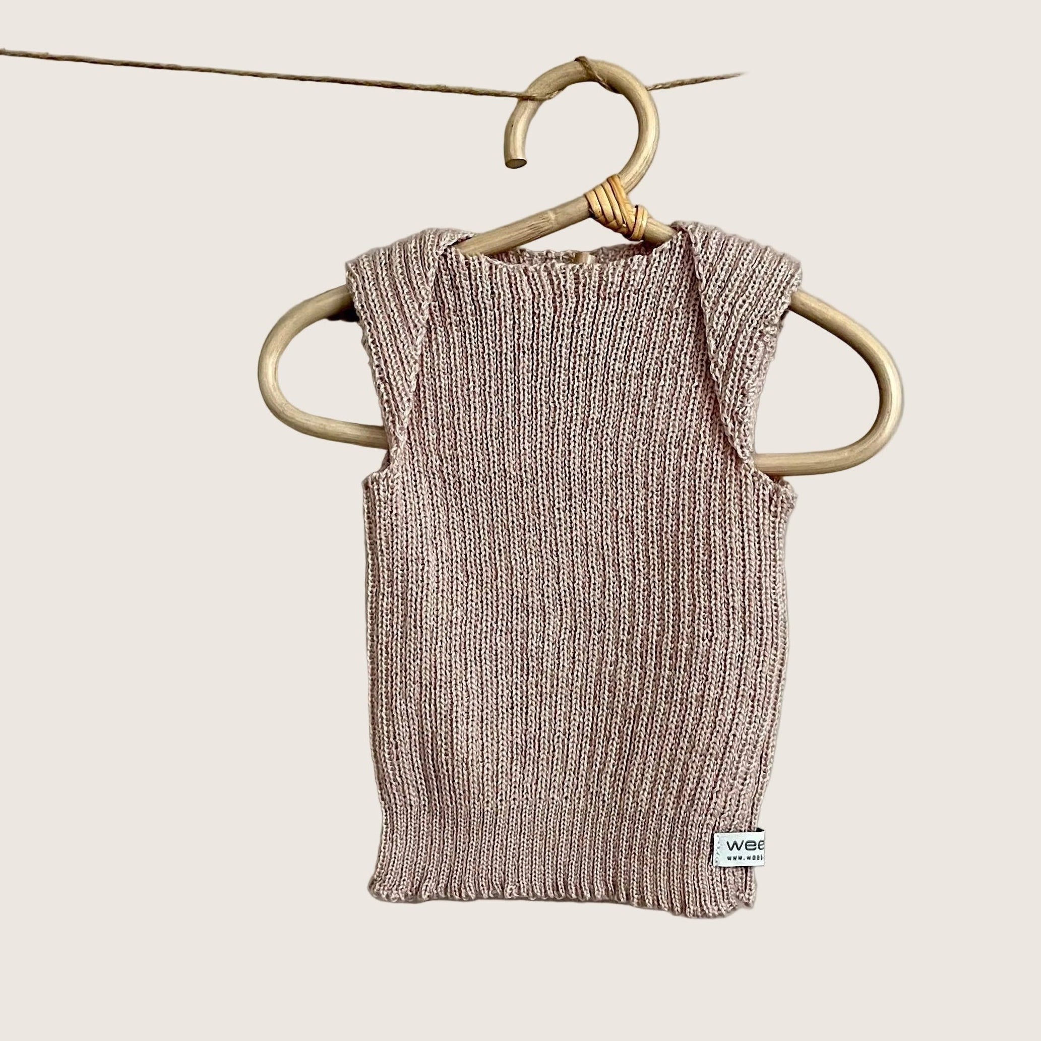 Knitted baby vest hanging on a hanger against a plain background