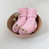Pair of pink baby socks in a wooden bowl on a light background