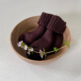 Pair of brown baby socks in a wooden bowl on a light background