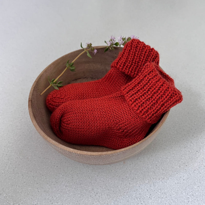 Pair of burnt orange baby socks in a wooden bowl on a light background