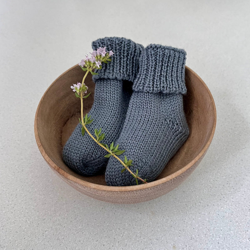 Pair of dusky blue baby socks in a wooden bowl on a light background