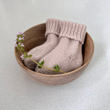Pair of sand baby socks in a wooden bowl on a light background