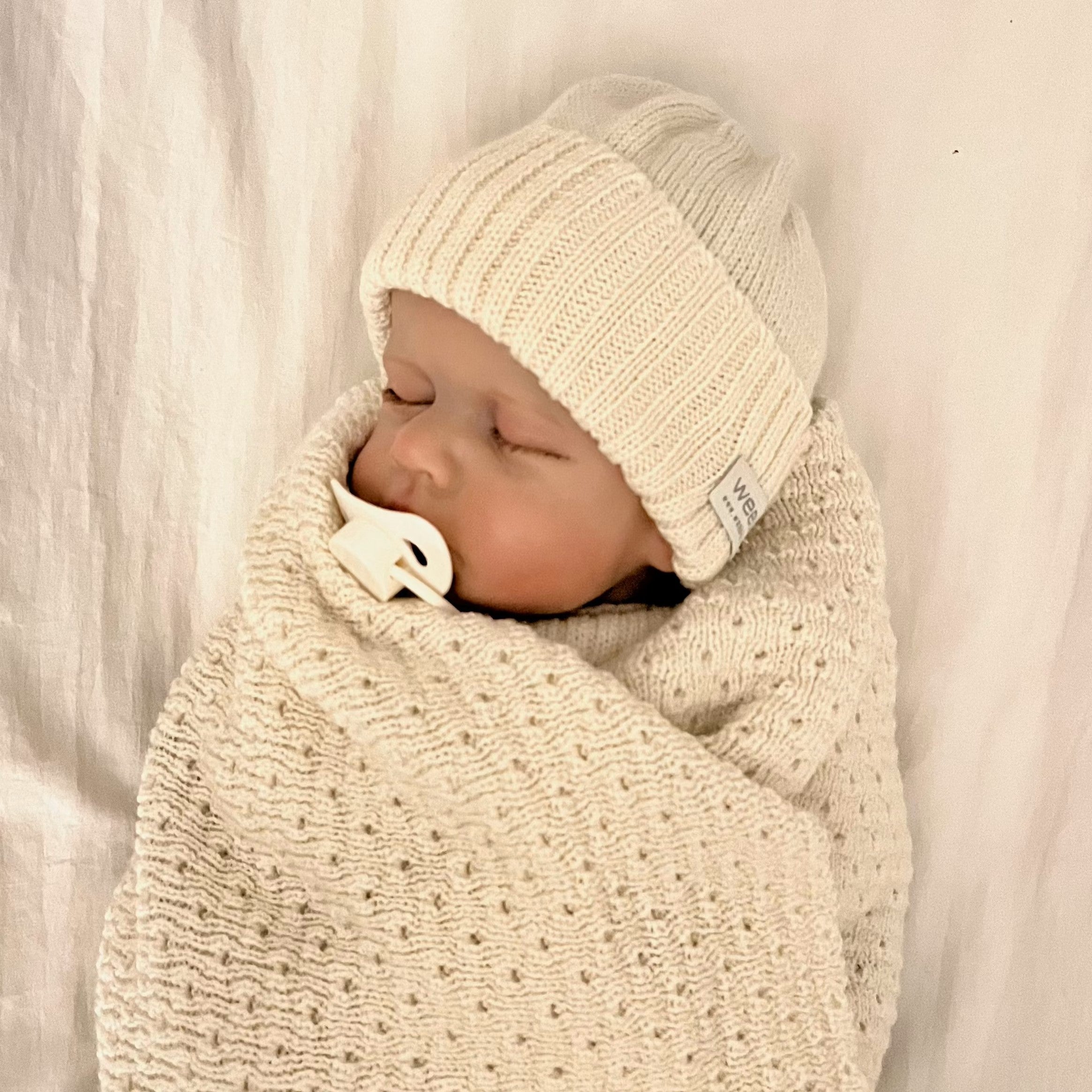 baby wrapped in cream blanket and matching beanie