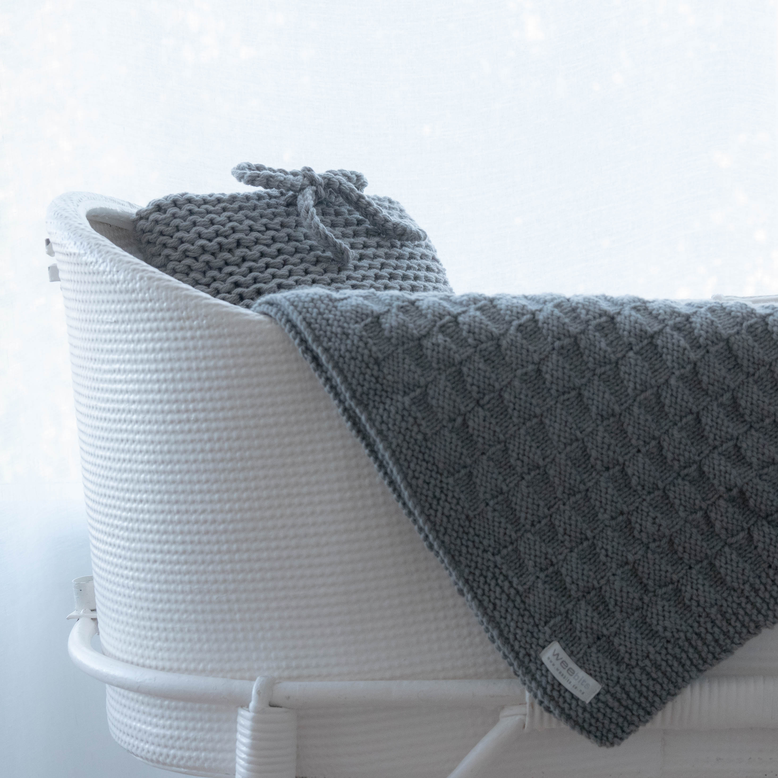 Gray textured blanket draped over a white woven basket on a light background
