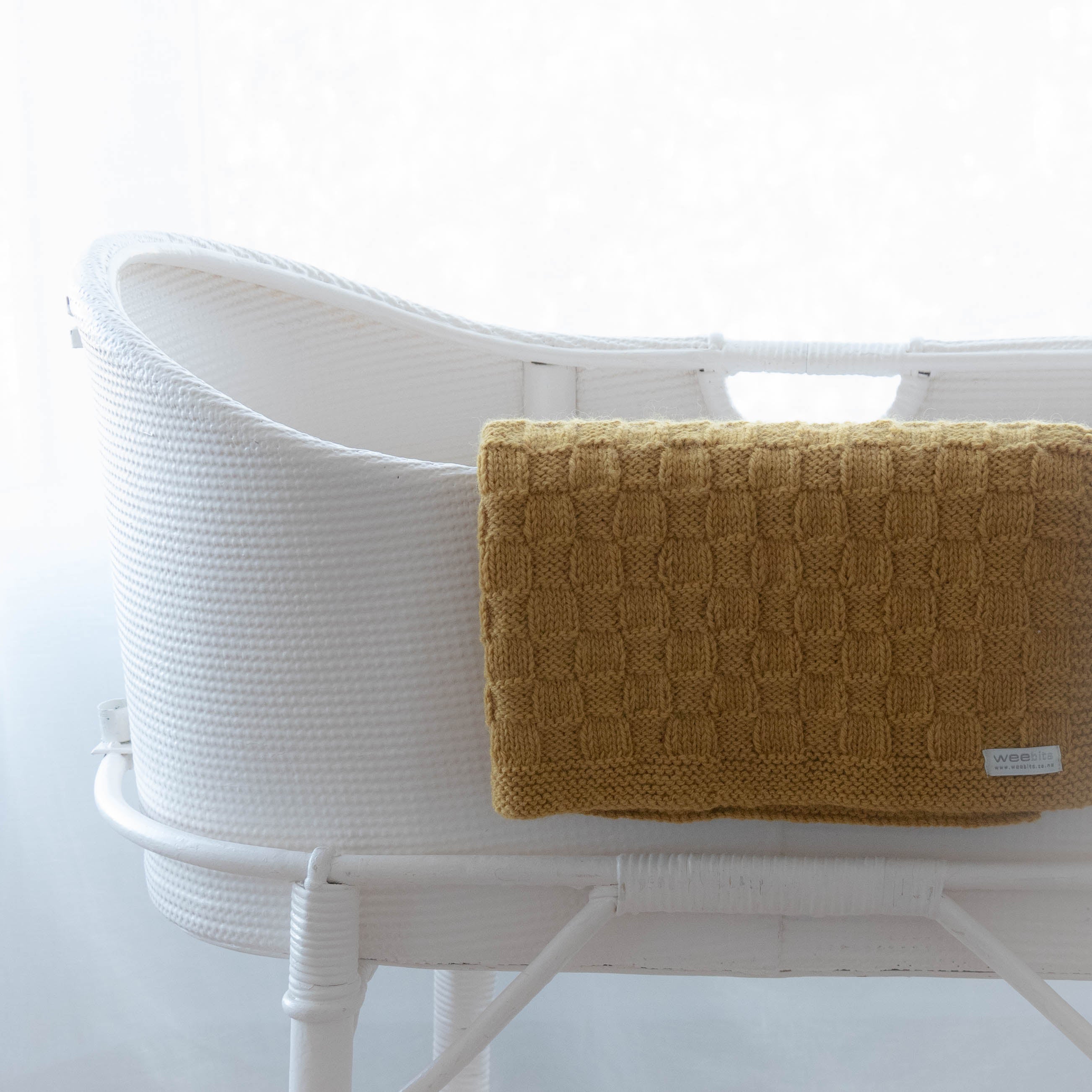 White woven basket with a mustard yellow textured blanket on a white background