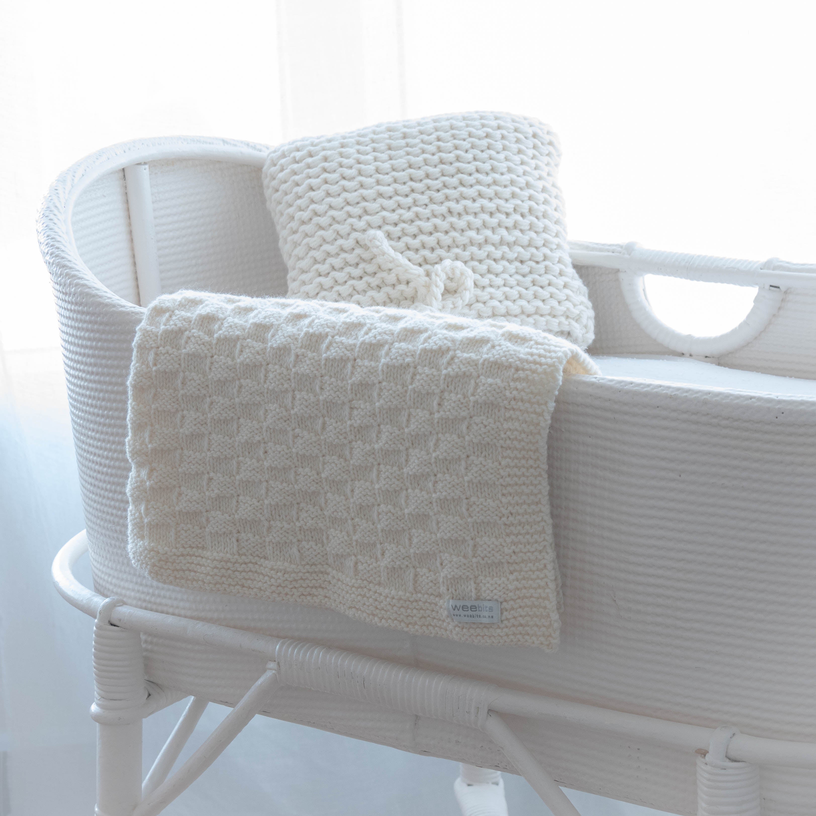 White textured blanket draped over a white wicker chair with a blurred white background