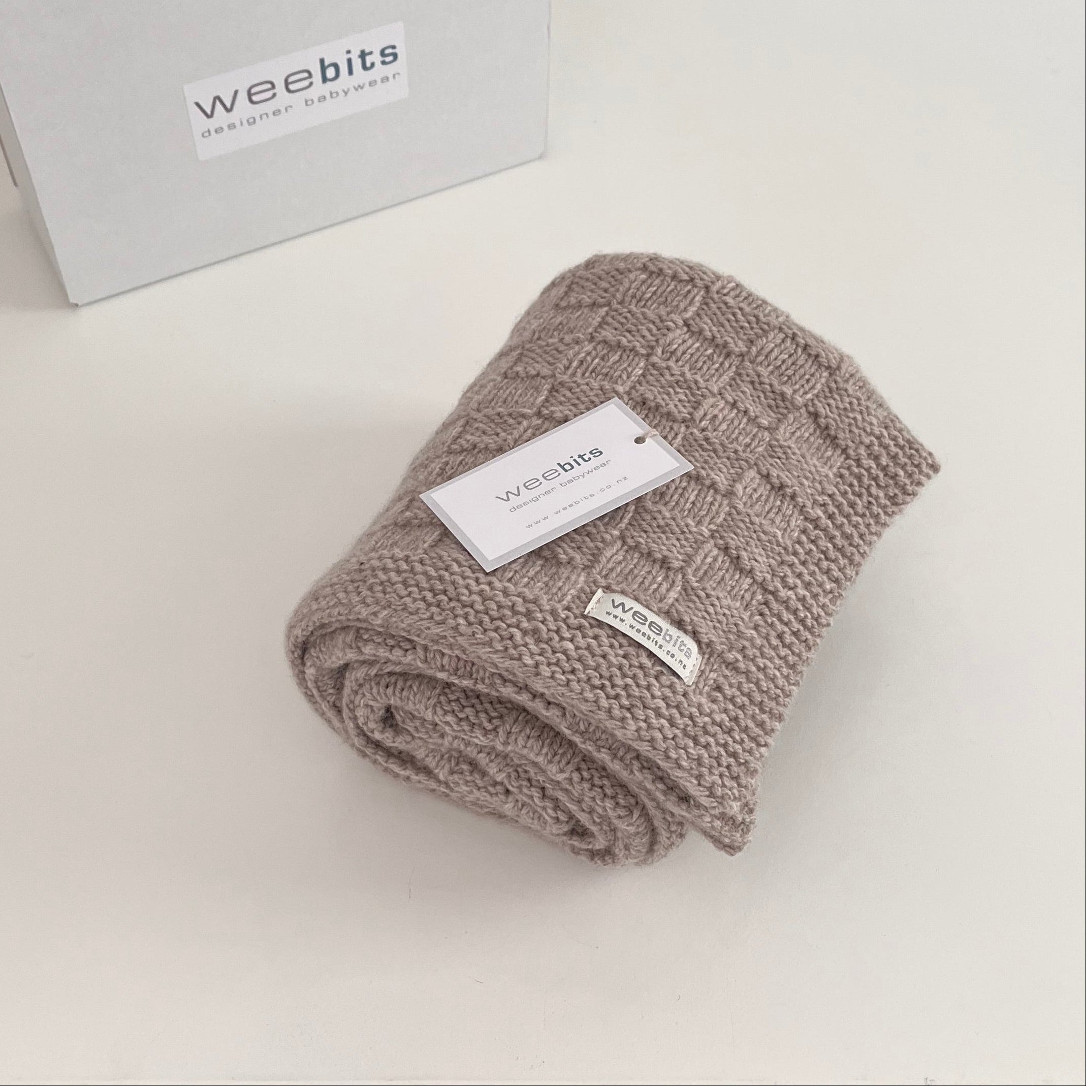 Folded knitted blanket with 'weebits' label on a light background