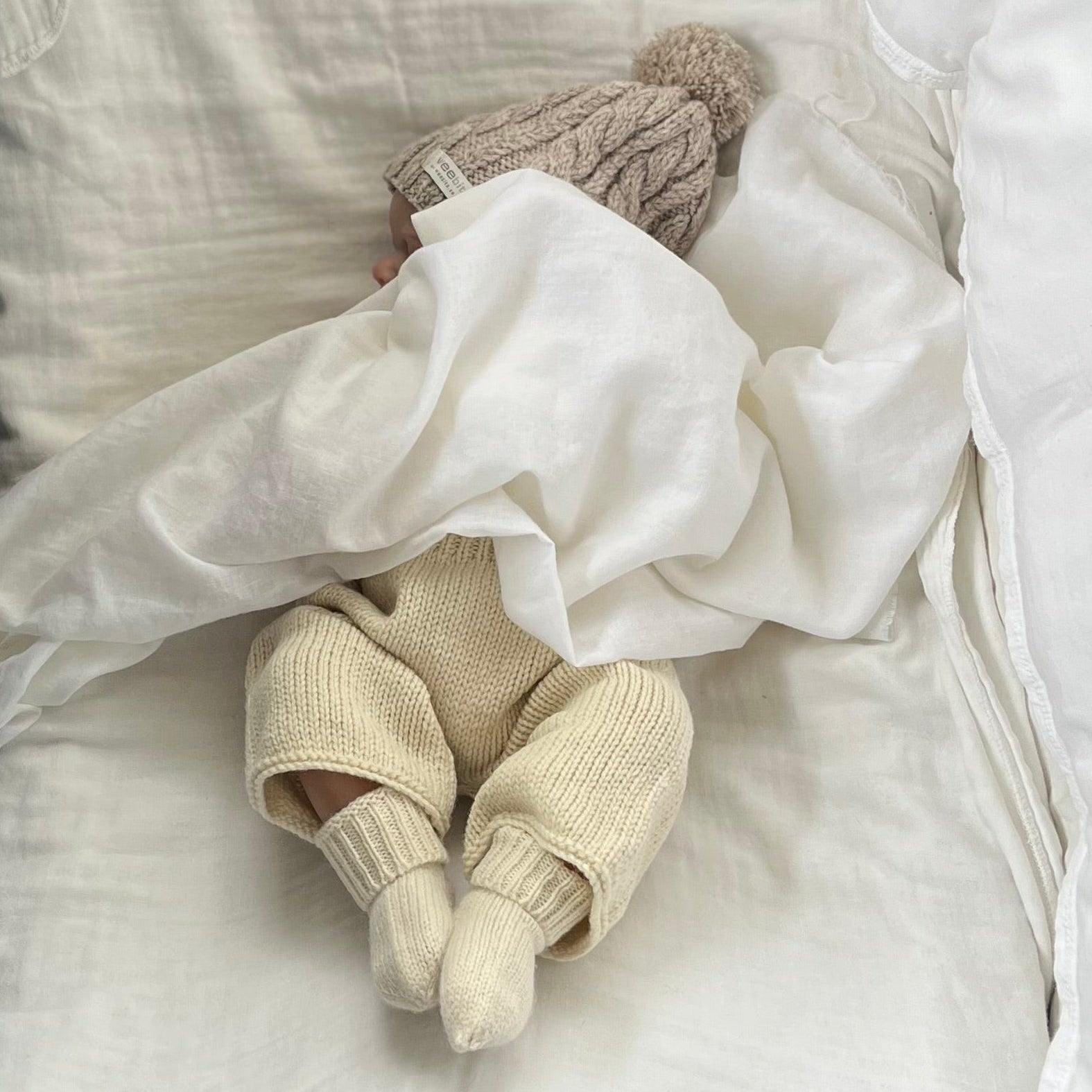 Newborn baby in knitted outfit wrapped in white blanket