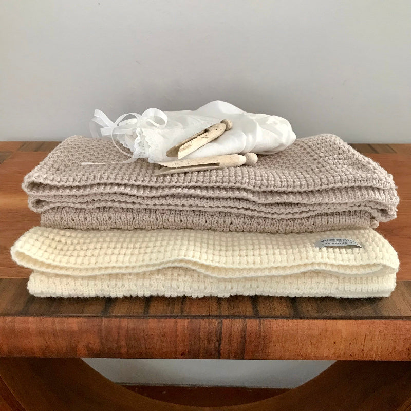 Stack of beige and cream textured bassinet blankets on a wooden surface with a neutral background