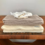 Stack of beige and cream textured bassinet blankets on a wooden surface with a neutral background