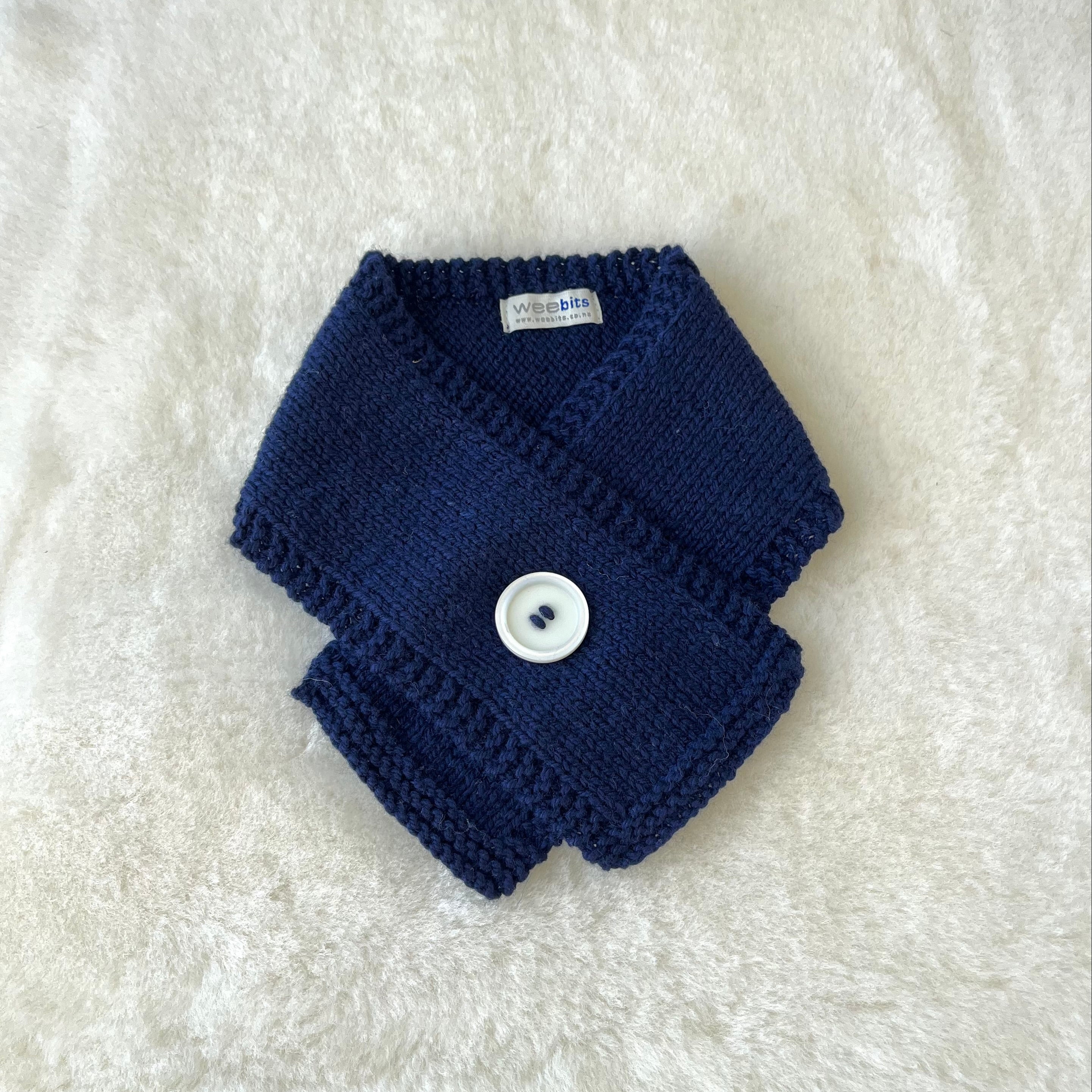 A light navy knitted baby scarf with a white button closure, laid flat on a white textured faux fur background.