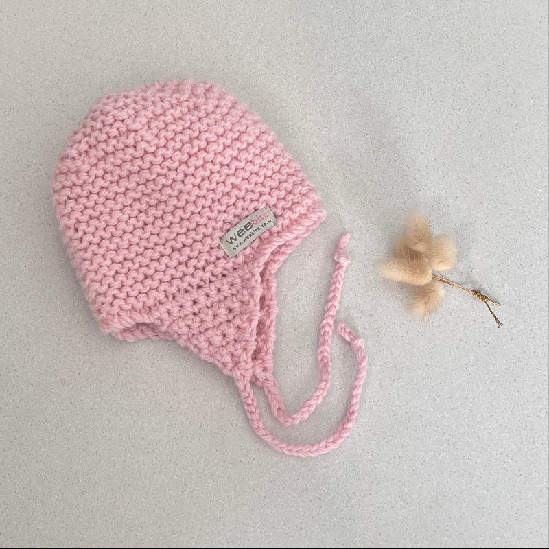 Knitted chunky knit baby hat pink colour on a light grey background