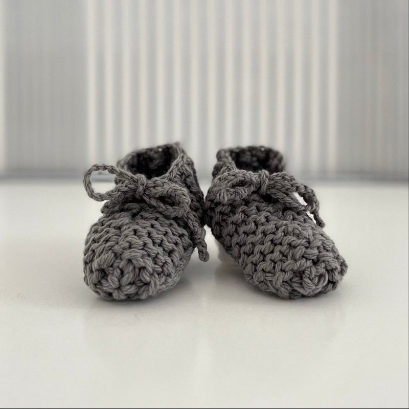 Pair of mushroom baby chunky knit booties on a white surface with a striped background
