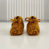 Pair of mustard baby chunky knit booties on a white surface with a striped background