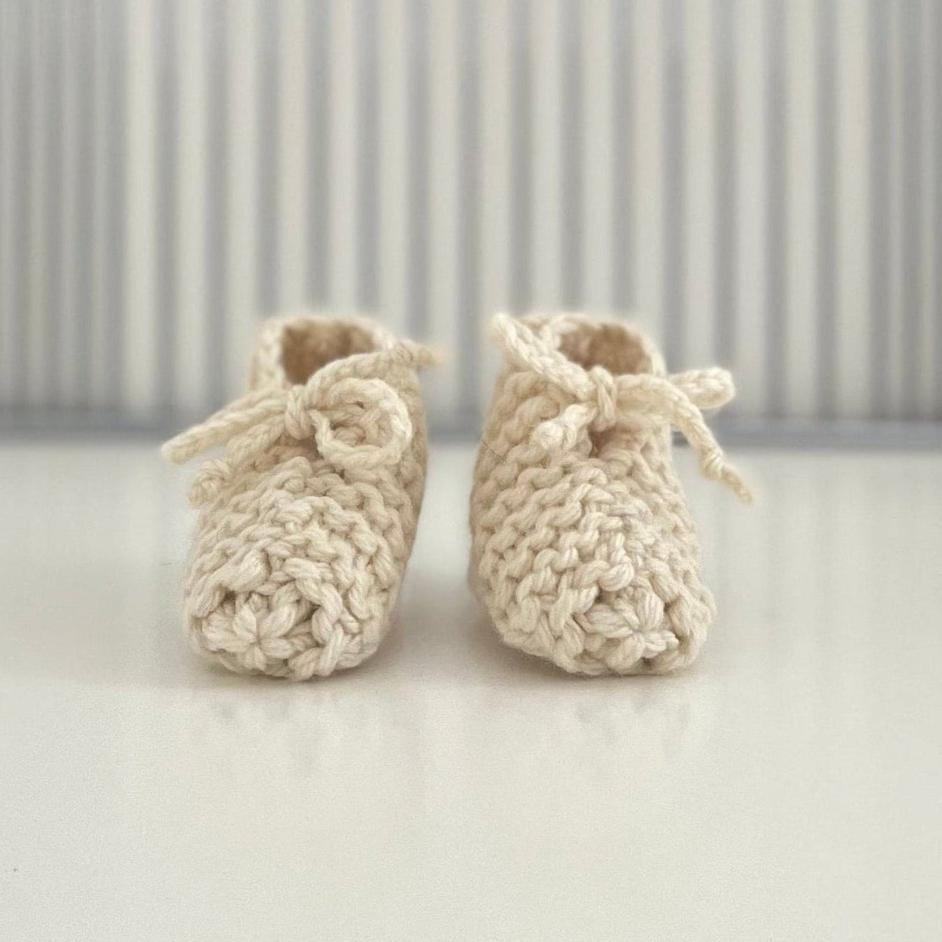 Pair of natural baby chunky knit booties on a white surface with a striped background