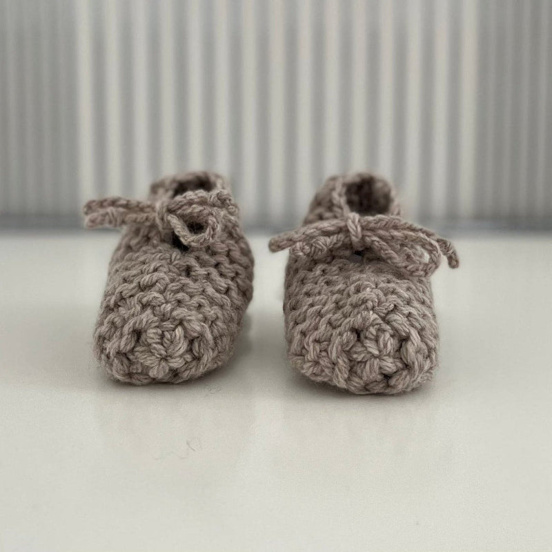 Pair of oatmeal baby chunky knit booties on a white surface with a striped background