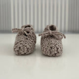 Pair of oatmeal baby chunky knit booties on a white surface with a striped background
