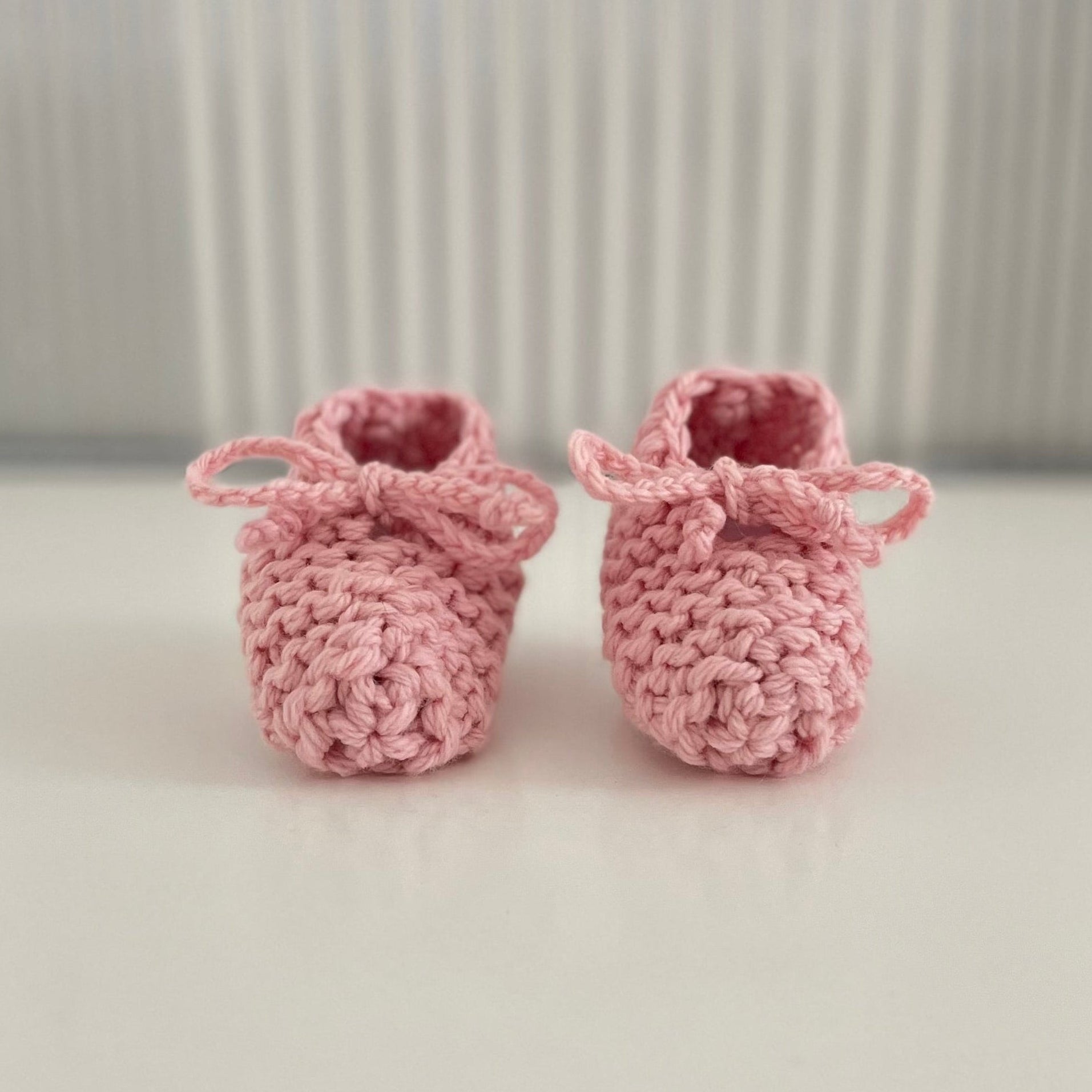 Pair of pink baby chunky knit booties on a white surface with a striped background