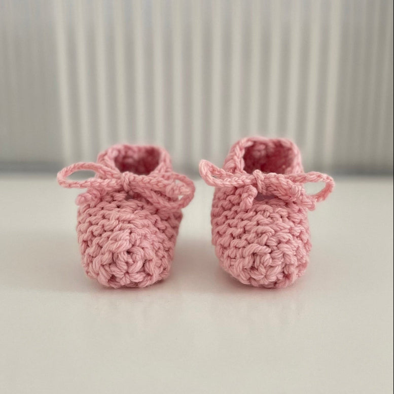 Pair of pink baby chunky knit booties on a white surface with a striped background