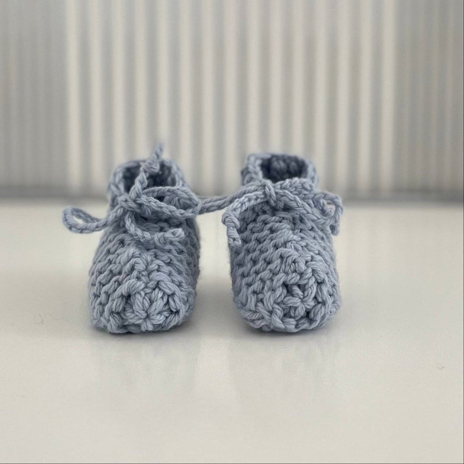 Pair of blue baby chunky knit booties on a white surface with a striped background